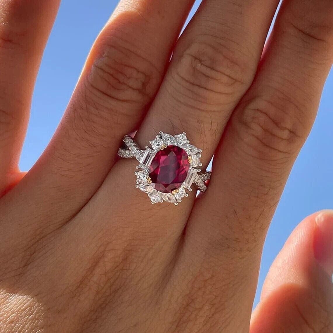 Woman's hand wearing an oval-cut red ruby engagement ring, showcasing its timeless elegance